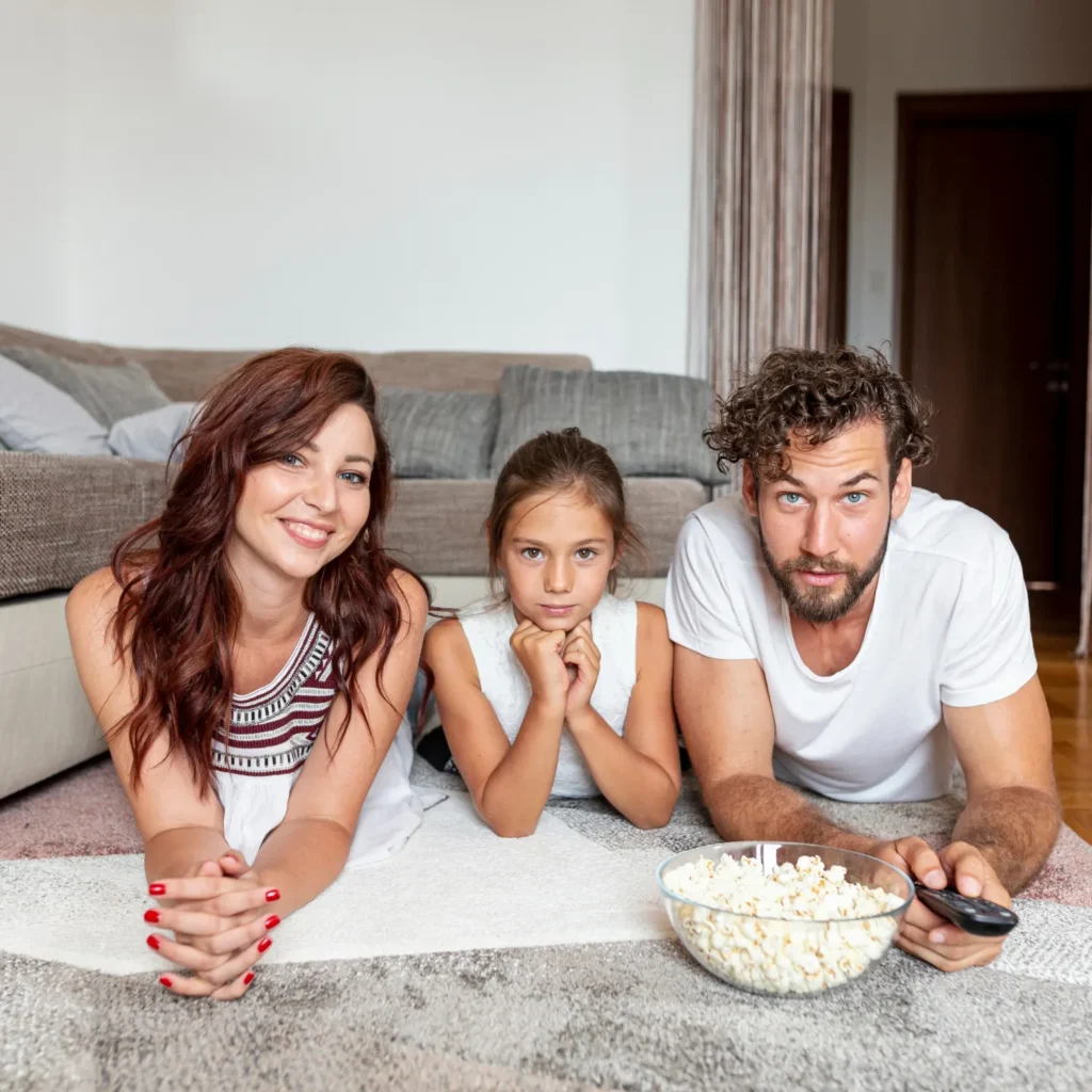 Famille regardant la télévision ensemble grâce à un test IPTV gratuit — parents et enfant allongés sur le tapis avec du popcorn