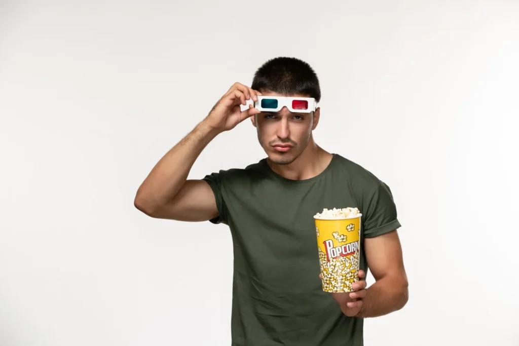 Jeune homme hésitant avec lunettes 3D et popcorn, illustrant l'importance de tester un abonnement IPTV 12 mois avant de s'engager

